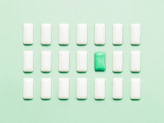 One green chewing gum  standing out of white chewing gums. Concept of individuality, uniqueness or loneliness, social outcast.