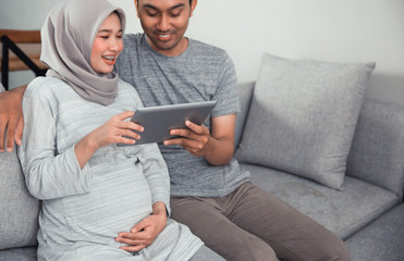 muslim pregnant woman using tablet pc with husband in livingroom