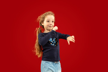 Beautiful emotional little girl isolated on red studio background. Half-lenght portrait of happy child smiling and dancing. Concept of facial expression, human emotions, childhood.