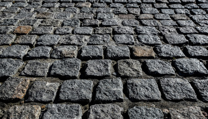 Black cobbled stone road background. Black or dark grey stone pavement texture. Ancient paving stone background
