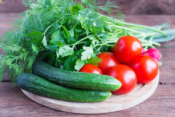 fresh cucumbers and tomatoes,radishes and greens on the table,ripe seasonal vegetables