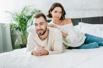 Fototapeta premium happy bearded man with clenched hands looking at camera with attractive woman while lying on bed