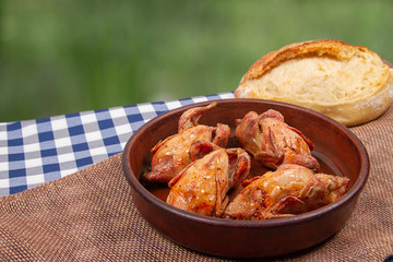 Roasted quail in clay pan and French white bread lie on the table outdoor
