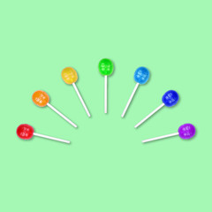 Set of colorful lollipops grouped in a half circle isolated on green background. Candy on a stick. Food background. Flat lay.