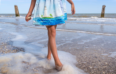 A girl in a beautiful dress and white hat on the seashore on a blue sky background
