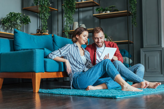 low angle view of happy man and woman looking at digital tablet in living room