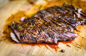 Sliced grilled juicy marinated beef flank steak on wooden board.