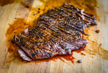 Sliced grilled juicy marinated beef flank steak on wooden board.