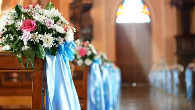 4K. interior view of empty church with wooden bench decorated with flower bouquet and blue ribbon blown by the wind, sunlight through church stained glass window