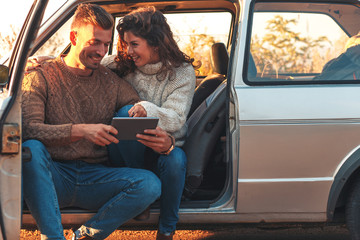 Beautiful couple on road trip, they are taking a break from driving and looking for direction on tablet.