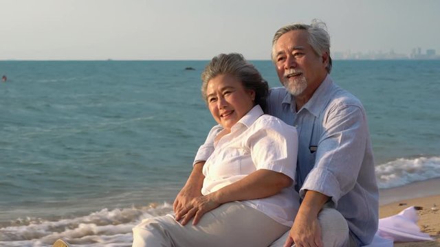 Asian couple senior sitting and relax summer on the beach together. Concept of happy family, post retirement, anniversary married, mental health and summer travel.