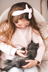 Blonde stylish kid girl 4-5 year old holding sleeping cat in room. Friendship. Childhood.