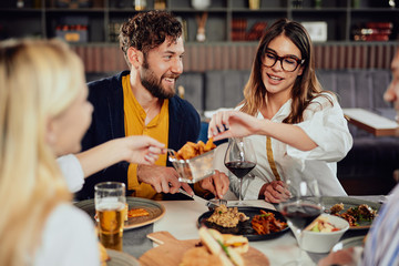 Multiethnic friends sitting at restaurant, drinking alcohol, chatting and having burgers for dinner.