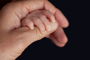 Father holding a newborn baby hand in his. Child hand closeup into parent hands together.