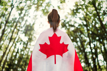 Child teenager girl at nature background an Canada flag on her shoulders  