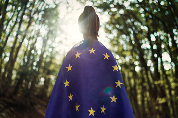 Child teenager girl at nature background an European Union flag on her shoulders  