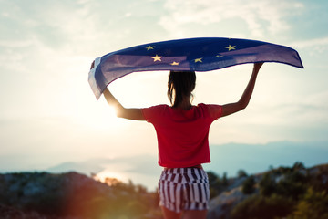 Child girl teenager young person is waving European Union flag on top of mountain at sky...