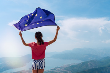 Child girl teenager young person is waving European Union flag on top of mountain at sky background - obrazy, fototapety, plakaty