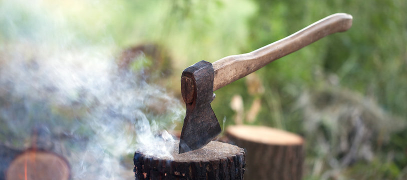 Axe in tree stump and campfire with smoke