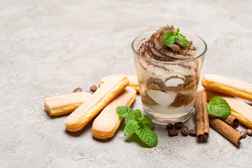 Classic tiramisu dessert in a glass and savoiardi cookies on concrete background