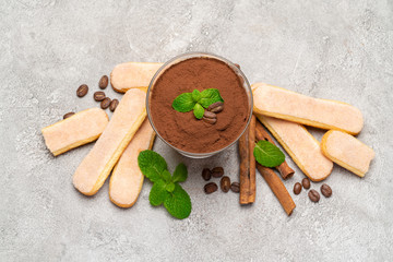 Classic tiramisu dessert in a glass and savoiardi cookies on concrete background