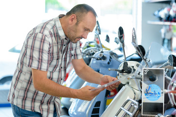 man looking at specifications of modern scooter in showroom