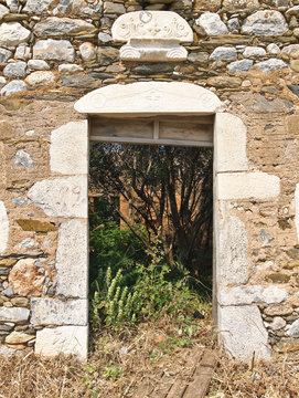 Building detail of fallen door on stone wall in Mani Greece with sybols above door opening.