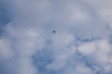 The plane is high in the blue sky with clouds from the bottom of the ground
