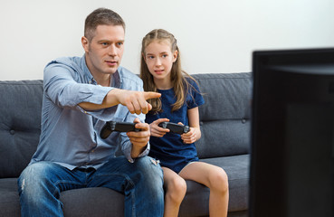 Father and daughter playing video game at home.