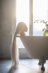 A beautiful woman with gorgeous long blond hair is relaxing in the bath. Silhouette of a woman in profile lying in the bathroom.
