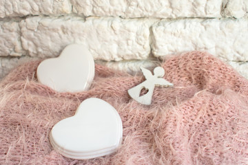 Figurine small angel with a porcelain heart on a pink blanket against the light wall