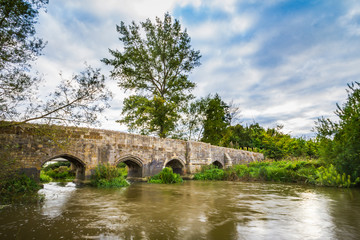 Fototapeta na wymiar Old stone medival bridge over a streaming river