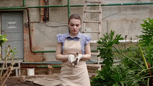 Woman gardener is walking in greenhouse satisfied with her work and putting off her gloves.