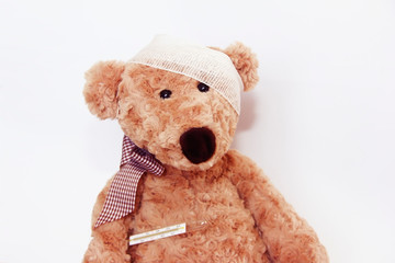 soft brown toy bear sick with a bandage on his head and a medical thermometer