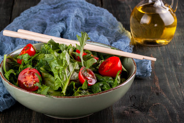 Salad with tomatoes, arugula and spinach on a black wooden table