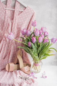 Delicate pink polka-dot dress and beige sandals with a bouquet of tulips. Clothes and shoes in a gentle style. Spring, summer mood.