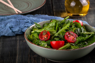 Salad with tomatoes, arugula and spinach on a black wooden table