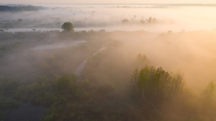Summer foggy dawn. Aerial background of spring river nature. Green field at morning sunrise.