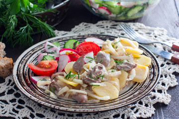 Cooked potatoes and chicken hearts on a plate with vegetable salad, horizontal