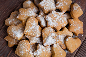 Homemade cookies in the shape of hearts and stars with icing sugar on a board in a pile on a brown wooden background, top view
