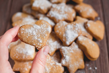 fingers hold homemade heart-shaped cookies on the background of a pile of cookies on a brown background, out of focus