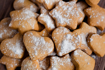 Fototapeta na wymiar Homemade cookies in the shape of a heart and stars with powdered sugar on a board on a brown wood background, closeup