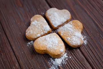 four heart-shaped cookies with icing sugar, luck symbol clover on a brown wooden background