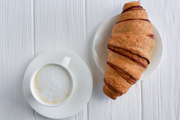 fresh croissant on a white wooden table with a cup of milk or cappuccino, top view