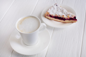 A piece of cake with blueberries, cappuccino, coffee, on a white wooden boards background