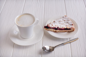 A piece of cake with blueberries, cappuccino, coffee, spoon, on a white wooden boards background
