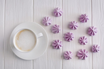 white cup of coffee, cappuccino on a white background with lilac meringues, top view