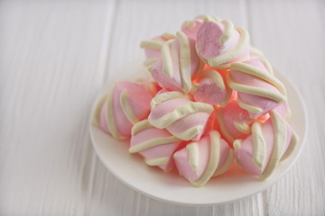 Fototapeta na wymiar pastel marshmallow flowers on a white saucer on a white wooden table