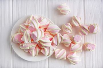 Fototapeta na wymiar pastel marshmallow flowers on a white saucer on a white wooden table, piled on the table, top view