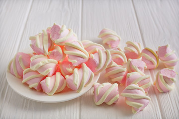 pastel marshmallow flowers on a white saucer on a white wooden table, piled on the table